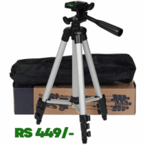 A silver and black portable camera tripod standing on a brown cardboard box, accompanied by a black nylon zippered carrying bag resting behind it.